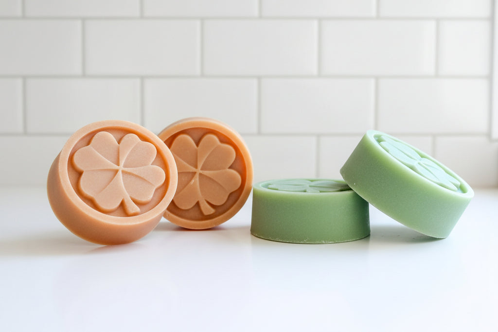 Four soap bars with four-leaf clover designs on a white surface