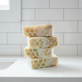 Stack of honeycomb-patterned soap bars on a white surface with a blurred natural background