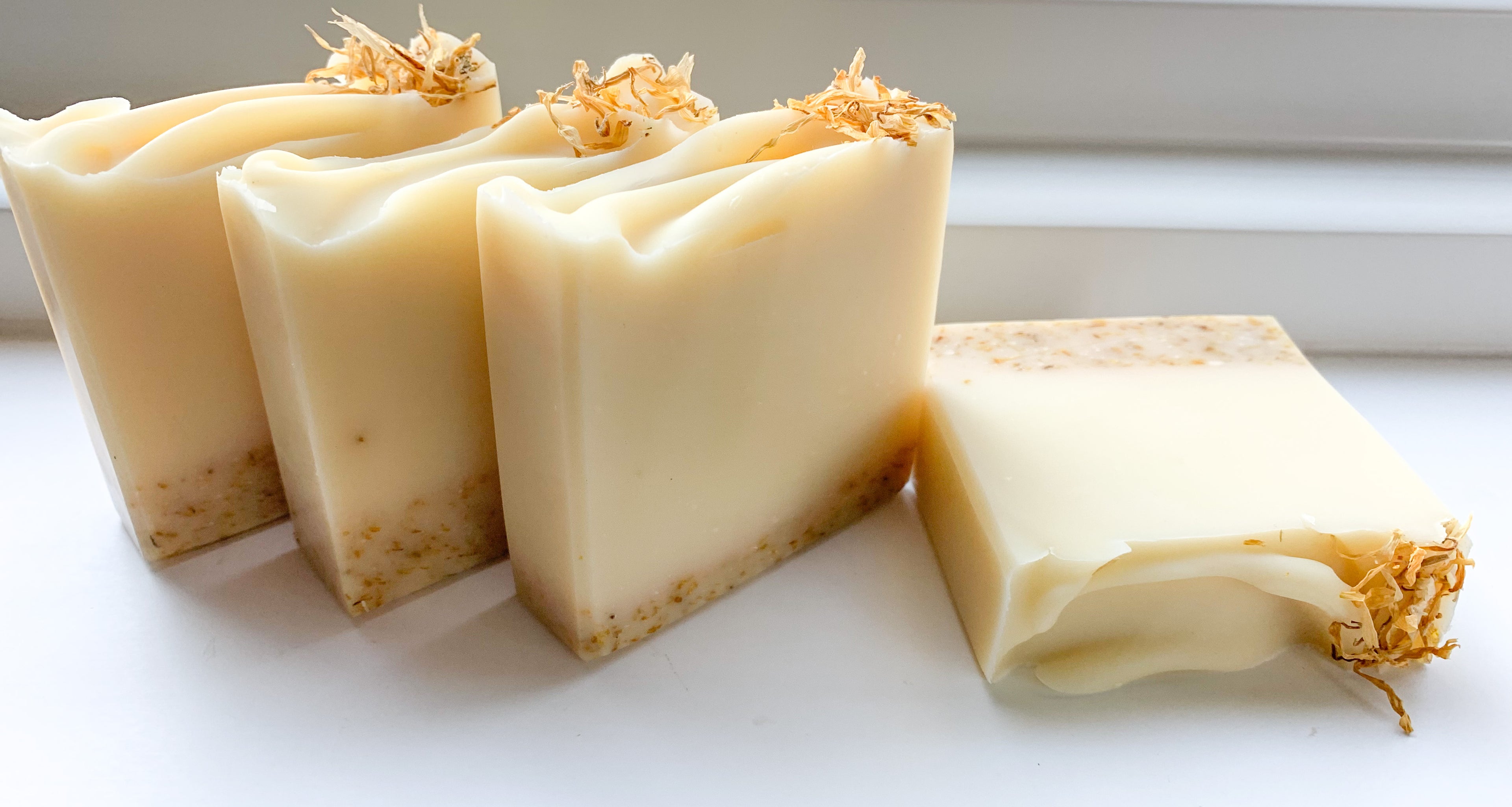 Four bars of soap with visible exfoliating elements from ground calendula, natural yellowish color from lemongrass essential oil