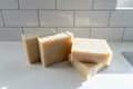 four bars of natural colored soap on a white counter with white tile background