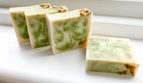 Four bars of soap with green swirl patterns on a white surface with dried Chamomile flowers on top