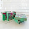 Four bar soaps with green, pink and white swirls on a white countertop