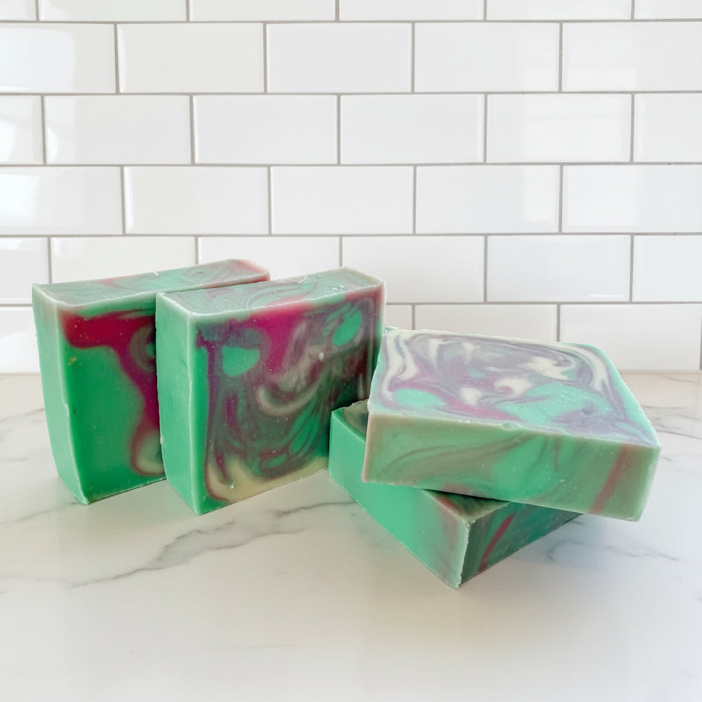 Four bar soaps with green, pink and white swirls on a white countertop