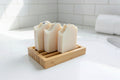 three bars of white soap with floral elements on wooden soap dish on a white surface