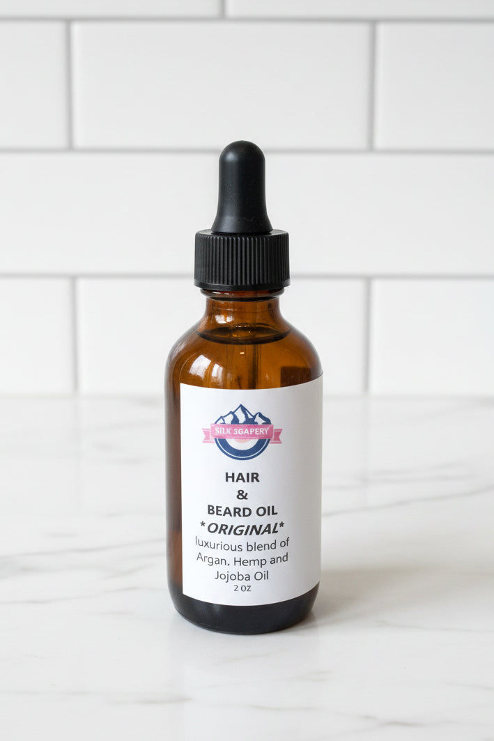A 2oz amber glass dropper bottle of Beard & Hair Original Beard Oil with a white label, set on a white ledge next to a window with strong natural sunlight casting a shadow.
