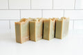 Four handmade soap bars with a light green-gray base and warm beige to golden-brown marbled swirls, arranged on a white surface.