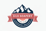Logo of Silk Soapery with mountains and a red banner on a white background